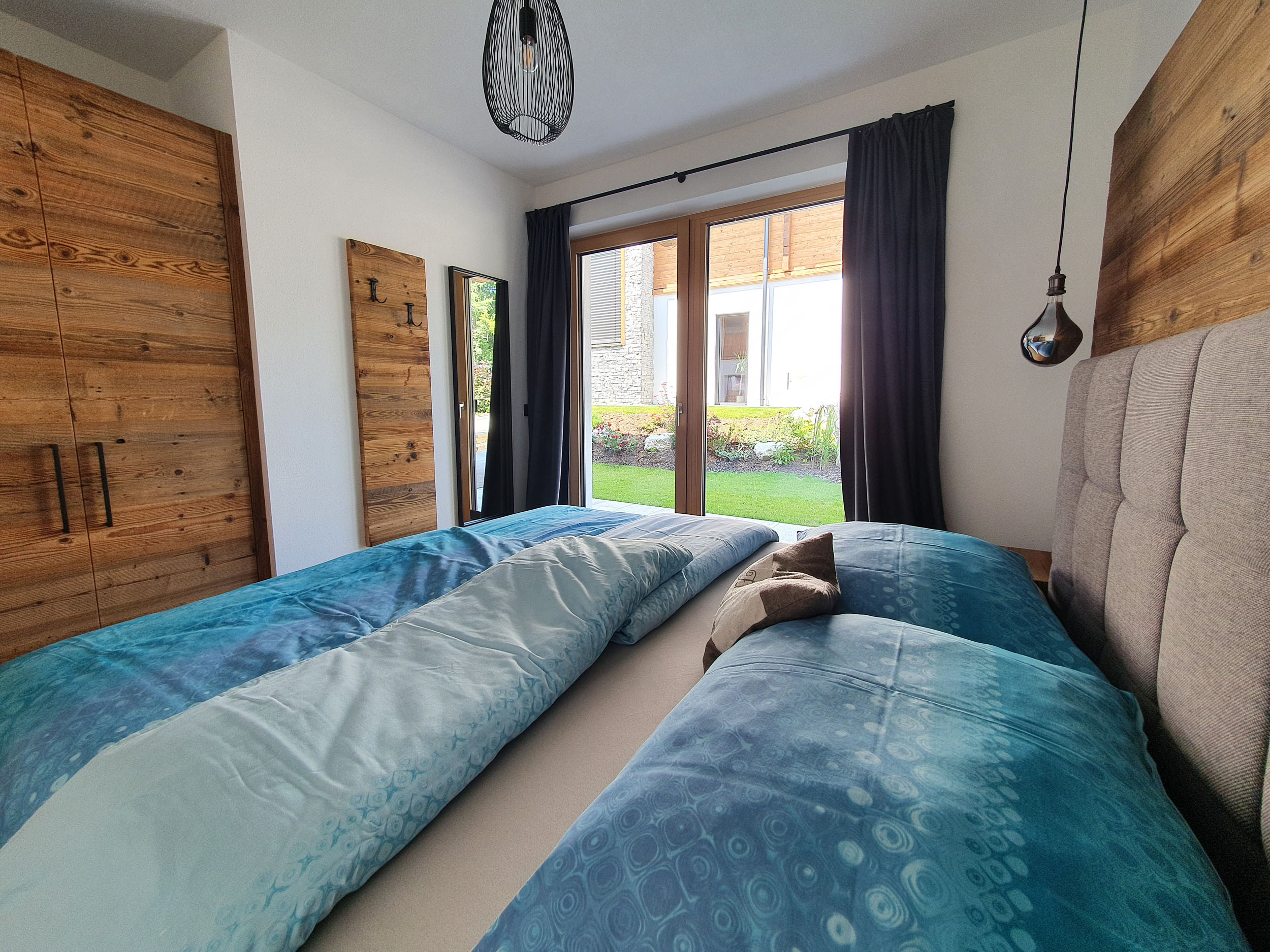 Boxspringbett mit türkis Decken, Panoramafenster und Altholzschrank im Chaletzimmer