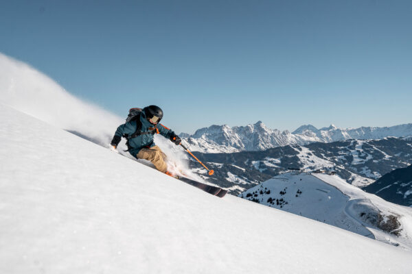 Ein Skifahrer fährt schwungvoll durch den frischen Pulverschnee mit weiter Sicht auf die umliegenden Berge.