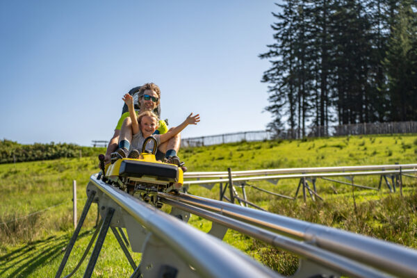 Vater und Kind genießen eine rasante Fahrt mit dem Sommer-Coaster an einem sonnigen Tag.