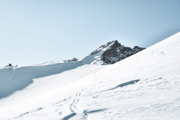 Verschneite Berglandschaft mit einem markanten Gipfel im Hintergrund, klare Fußspuren führen durch die unberührte Winterlandschaft unter wolkenlosem Himmel.
