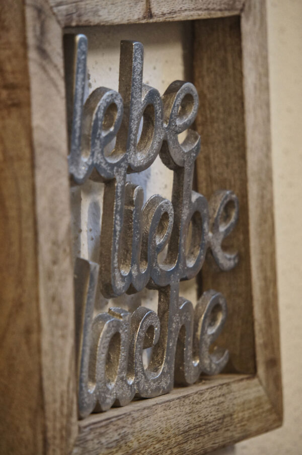 Dekoratives Wandbild aus Holzrahmen mit silberner Schrift „lebe liebe lache“ im rustikalen Chalet-Ambiente.