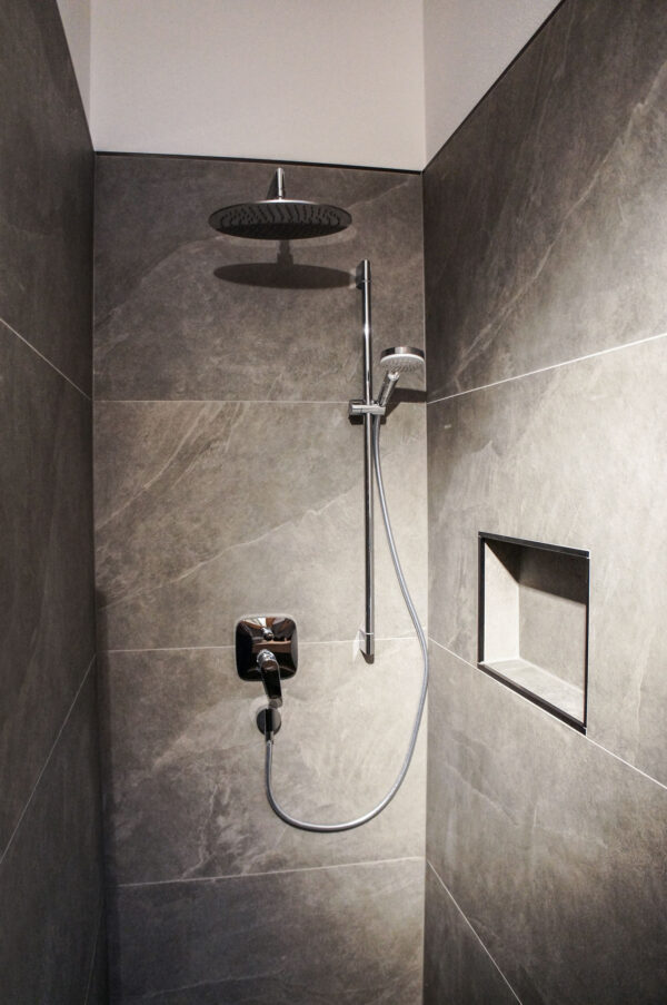 Moderne Dusche mit Regenduschkopf, Handbrause und Nische in elegantem Bad mit grauen Feinsteinzeugfliesen