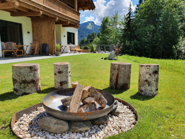 Runde Baumstamm-Sitzhocker um Feuerschale vor Chalet