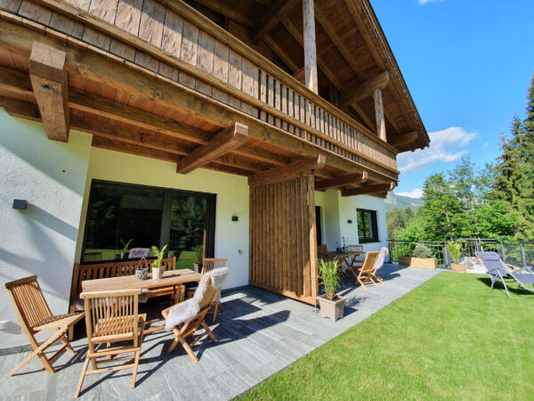 Überdachte Holzterrasse mit Esstisch und Bergwiese