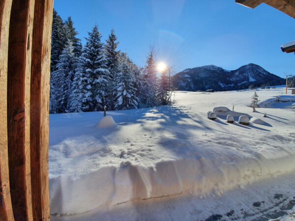 Blick von Holzterrasse auf verschneite Wiese unter strahlender Wintersonne