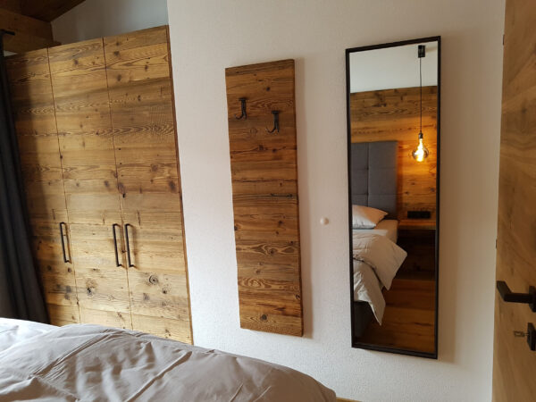 Spiegelwand reflektiert Boxspringbett und Altholzschrank im Chalet-Schlafzimmer