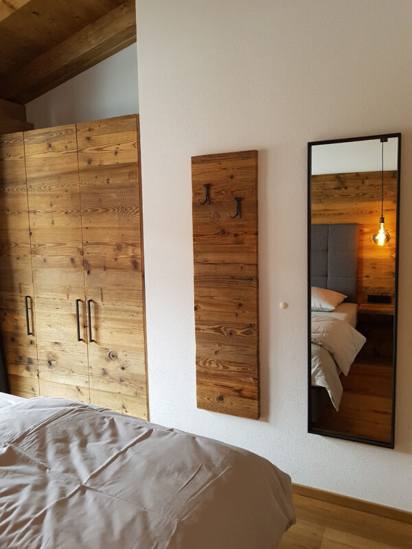 Hoher Spiegel und Altholzschrank neben Bett im Schlafzimmer