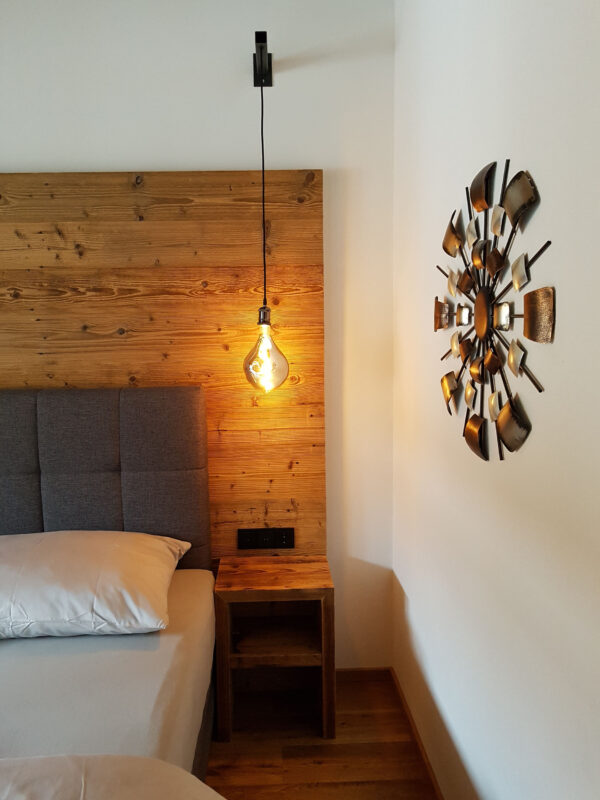 Pendelleuchte, Boxspringbett und Sonnenrad-Deko schaffen Chalet-Ambiente