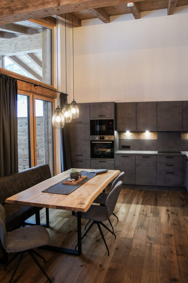 Offene Küche mit Esstisch aus Holz, modernen Hängelampen und großem Fenster mit Blick auf die Terrasse