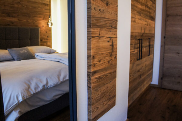 Seitlicher Blick ins Schlafzimmer mit Doppelbett, Spiegelelement und raumhohem Holzkleiderschrank