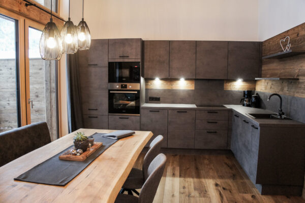 Moderne Einbauküche in Betonoptik mit Holzdetails, Esstisch und Pendelleuchten in offener Wohnküche
