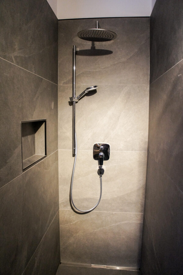 Begehbare Dusche mit Regenduschkopf, Handbrause und integrierter Nische in grauen Steinfliesen