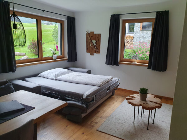 Ausziehbare Schlafcouch im Wohnbereich vor Panoramafenster mit Blick ins Grüne.
