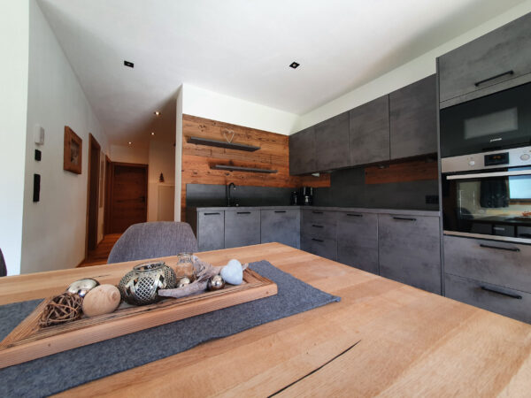 Moderne Chaletküche mit grauen Fronten, Altholzregal und großem Holzesstisch