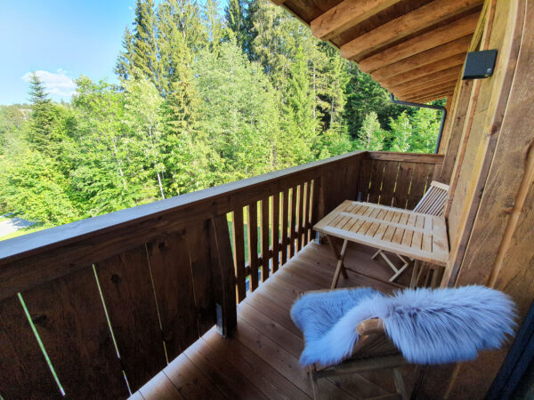 Holzbank am Balkon mit grüner Waldkulisse im Hintergrund