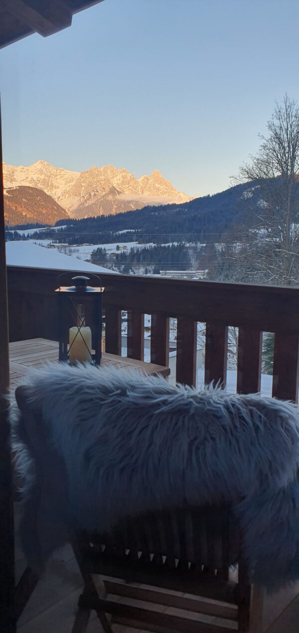 Balkon im Winter mit Fell, Laterne und Alpen-Bergblick bei Sonnenuntergang