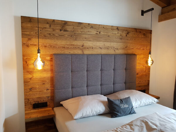 Boxspringbett vor Altholzwand und warmen Pendelleuchten im Schlafzimmer