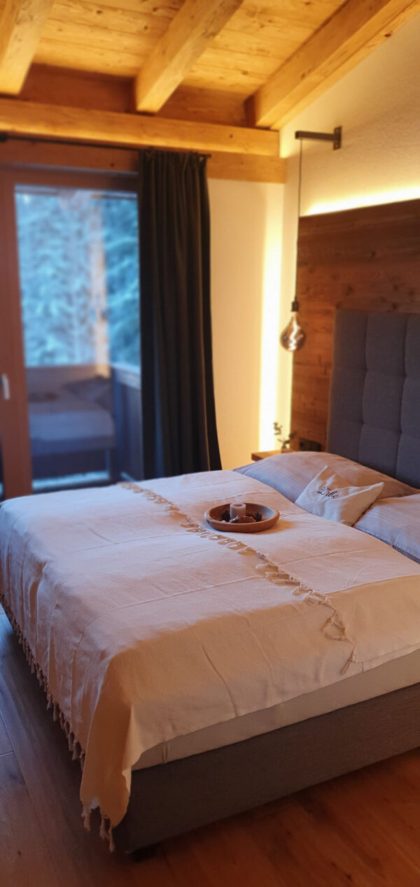 Boxspringbett mit heller Tagesdecke unter gemütlichem Warmlicht im Chalet