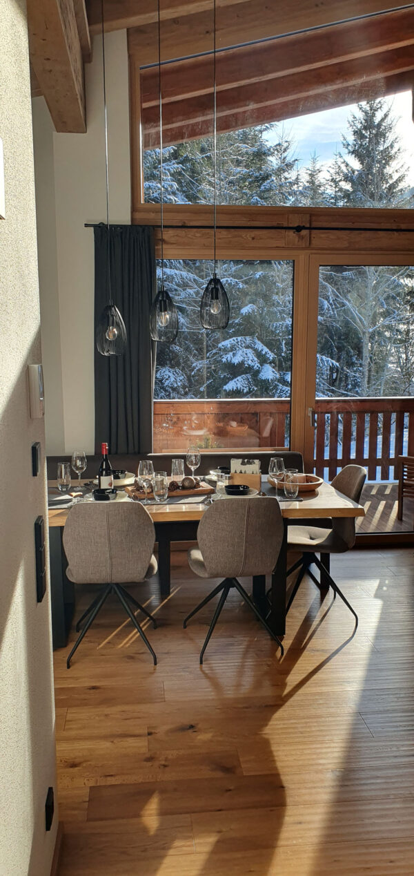Essbereich mit Holztisch, Balkonzugang und schneebedeckten Fichten