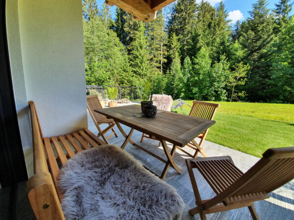 Holzbalkon-Lounge mit Tisch, Fellauflage und Blick auf Sommerwiese