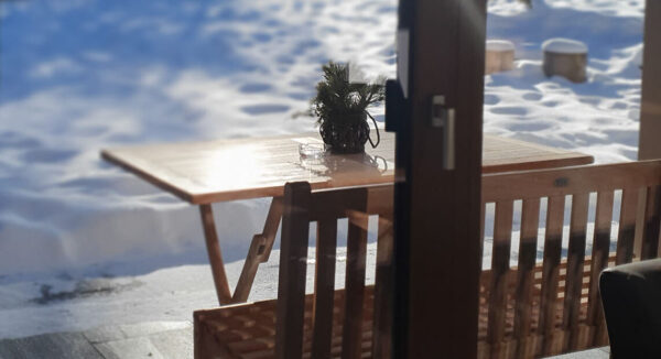 Wintersonne strahlt auf Holzterrasse mit Bank und Schneefeld im Blick