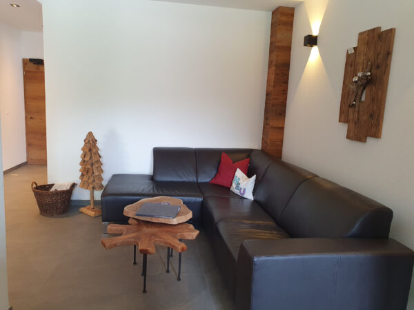 Wohnzimmer im Chalet zeitfrei Fieberbrunn mit gemütlichem Ledersofa und dekorativen Holztischen – Entspannung pur in den Kitzbüheler Alpen.
